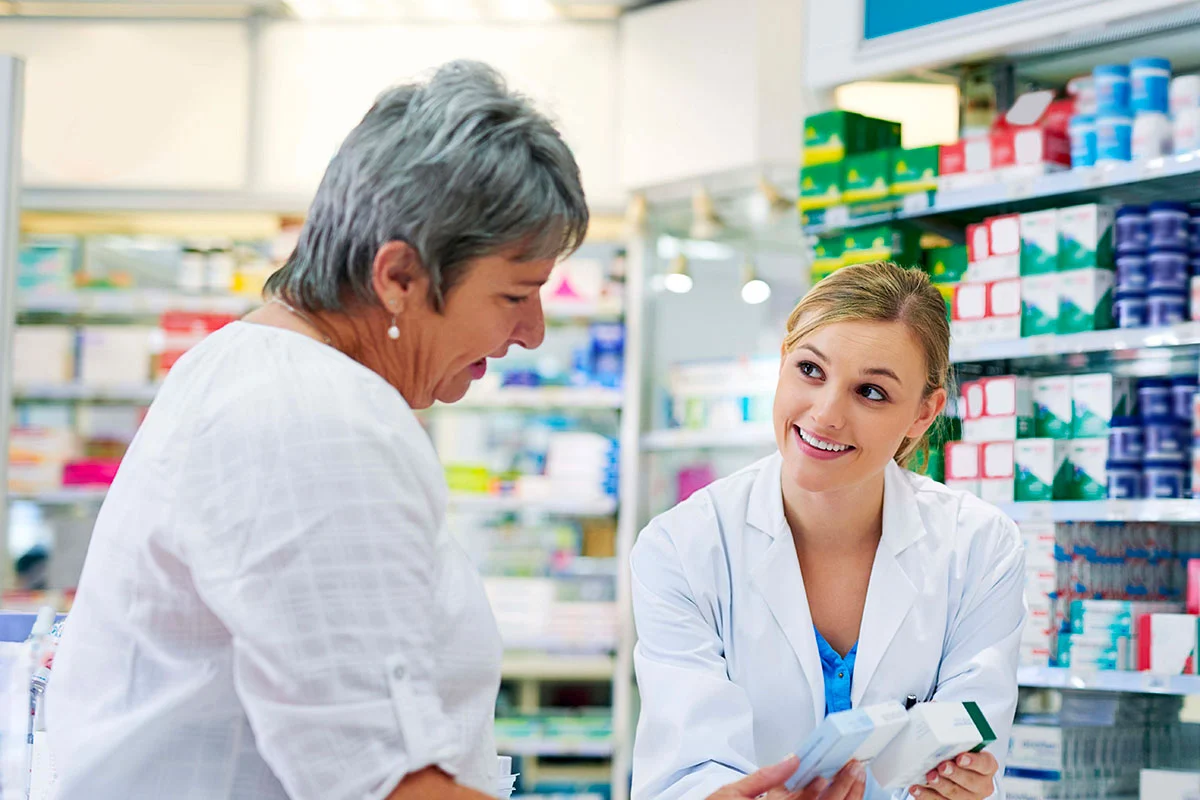 Smiling woman in white medical coat showing customer to medical boxes